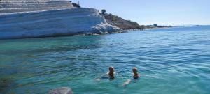two people swimming in the water near a cliff at Appartamento Alla Marmora Porto Empedocle in Porto Empedocle