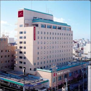 a large white building with a red sign on it at Nest Hotel Matsuyama in Matsuyama