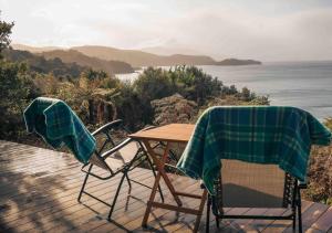 two chairs and a table on a deck with the ocean at Hananui PurePod in Stewart Island