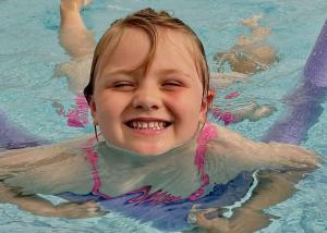 a young girl is smiling in a swimming pool at Orchards Holiday Park in Newbridge
