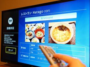 a person holding a remote control in front of a tv with food at Dormy Inn Premium Kyoto Ekimae Natural Hot Spring in Kyoto