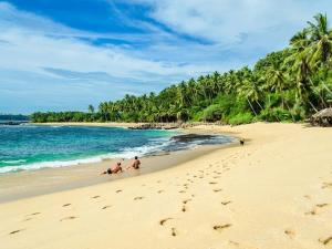two people sitting on a beach near the ocean at Swarnapaya résidence in Bentota