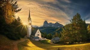 a church in the mountains with the sun shining on it at Muller Private Rooms in Ortisei