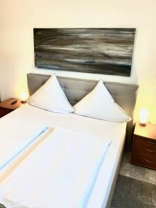 ein Bett mit weißen Kissen und ein Gemälde an der Wand in der Unterkunft Lüttje Huus Frieda mit Strandkorb am Strand von Mai bis September in Cuxhaven