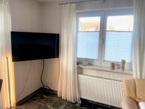 a living room with a flat screen tv and two windows at Lüttje Huus Frieda mit Strandkorb am Strand von Mai bis September in Cuxhaven