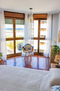 Schlafzimmer mit einem Bett, einem Stuhl und Fenstern in der Unterkunft MyHouseSpain - Playa de poniente, con vistas al mar y parking gratuito in Gijón