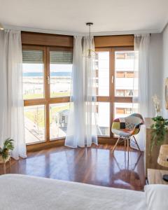 ein Schlafzimmer mit einem Bett und einem Stuhl sowie einem großen Fenster in der Unterkunft MyHouseSpain - Playa de poniente, con vistas al mar y parking gratuito in Gijón