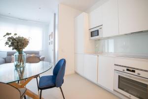 a white kitchen with a glass table and blue chairs at MyHouseSpain - Nuevo apartamento junto al Bernabéu in Madrid