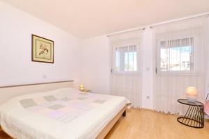 een witte slaapkamer met een bed en 2 ramen bij Apartments Vanda in Mali Lošinj