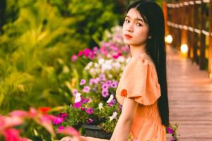 een vrouw in een oranje jurk op een houten loopbrug met bloemen bij Nakara Villas & Glamping Udon Thani in Udon Thani