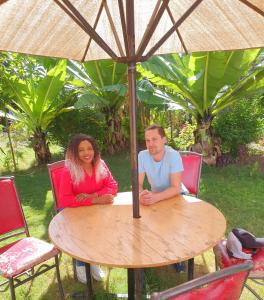 un homme et une femme assis à une table sous un parapluie dans l'établissement Homebase gardens, à Nakuru