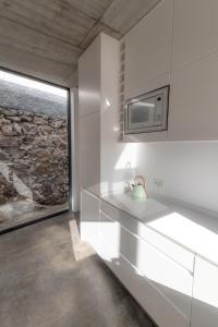 uma cozinha com armários brancos e uma parede de pedra em CASA DA PITANGA em Jardim do Mar