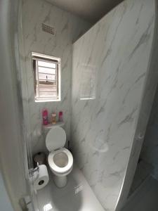 a white bathroom with a toilet and a window at Kasuda Rooms - Cosy self contained rooms in Livingstone