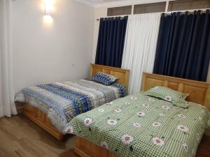 two beds in a bedroom with blue curtains at Stand alone gateway in Kampala