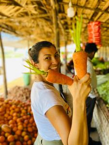 a woman holding up two carrots in a market at SAYON RIVER COTTAGE & ECO GARDEN in Monaragala