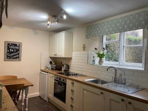 a kitchen with white cabinets and a sink and a window at Gingerbread Cottage in Chideock