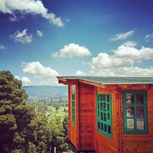 een houten huis met groene ramen op een heuvel bij Huitaca Glamping in Paipa