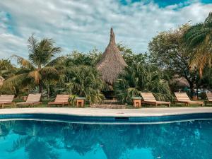 a resort with a swimming pool with chairs and a thatched building at The Happy Coconut Resort in Tola