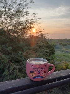 a coffee cup sitting on a balcony with the sunset at ไร่ดง โฮมเสตย์ in Ban Pong Nua