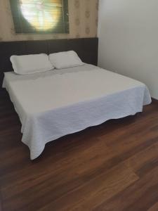 a bed with a white blanket on a wooden floor at Kitnet na Rua Sapucai in Belo Horizonte