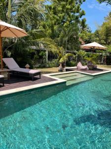 a pool with chairs and umbrellas next to a resort at Kaien Villas Gili Air in Gili Islands