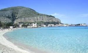 a beach with blue water and a mountain in the background at Da Rosina in Palermo