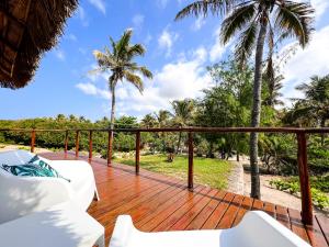 a wooden deck with white furniture and palm trees at Kumba Lodge in Praia do Tofo