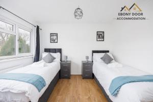 two beds in a room with white walls and wooden floors at Ebony Door Serviced Accommodation Barking Riverside in Barking