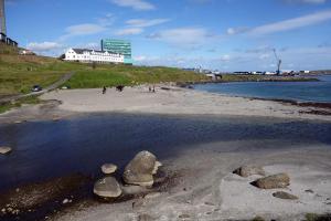 a beach with rocks in the water and a building at Autocamper Tórshavn in Tórshavn
