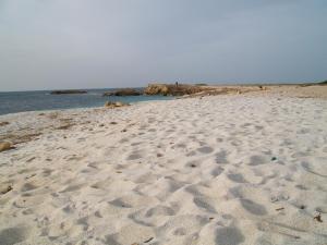 una playa con huellas en la arena y el océano en Notte di Luna room & breakfast, en Oristano