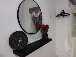 a mirror and a clock on a shelf with roses at Dahliya Roomstay Langkawi in Pantai Cenang