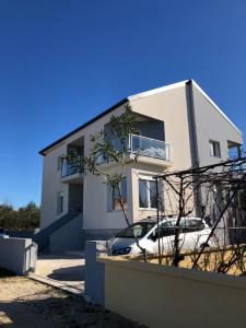 a white house with a car parked in front of it at Apartments Villa Prima in Privlaka