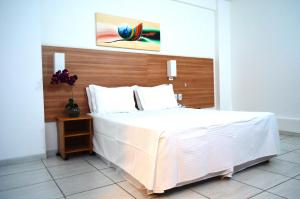 a bedroom with a large white bed with a wooden headboard at Hotel Áster in Alagoinhas