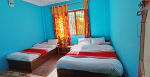 two beds in a room with blue walls and a window at Patlekhet Eco Farmhouse in Dhulikhel