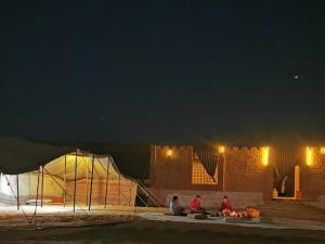 un groupe de personnes assis sous une tente la nuit dans l'établissement Desert Wonders Camp, à Ḩawīyah