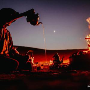 una persona está sentada alrededor de una fogata con una bebida en Bivouac Karim Sahara, en Zagora