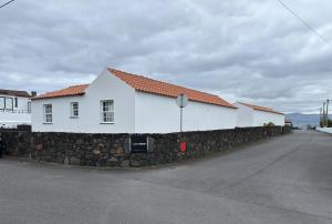 un edificio blanco con una pared de piedra junto a una calle en Casas do Verdelho, en Madalena