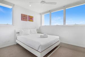 a white bedroom with a bed with white sheets and windows at Modern Contemporary Southport Apartment in Gold Coast