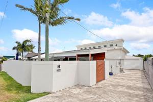 a white house with a fence and a palm tree at Mooloolaba Oasis 4bd Home, Pool in Mooloolaba