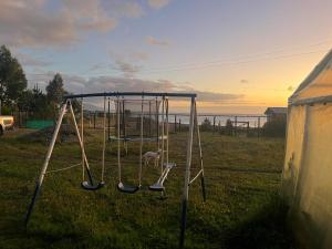 a swing set in a field with the sunset in the background at Cabaña Quillaipe orilla del mar in Puerto Montt