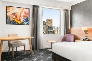 a hotel room with a bed and a desk and a window at Furama Darling Harbour in Sydney