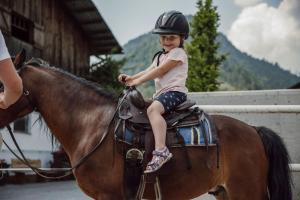 mały chłopiec siedzący na koniu w obiekcie Landhotel Lerch Plankenau w mieście Sankt Johann im Pongau