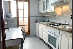 uma cozinha com armários brancos e um forno com placa de fogão em Apartamento con terraza en 1ª linea lateral a mar em Calafell