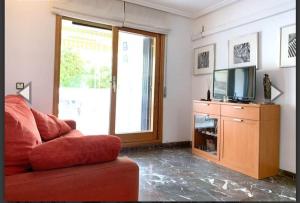 uma sala de estar com um sofá vermelho e uma televisão em Apartamento con terraza en 1ª linea lateral a mar em Calafell