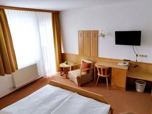 Habitación de hotel con cama, escritorio y TV. en Hotel Gästehaus Neubauer en Kaltenberg