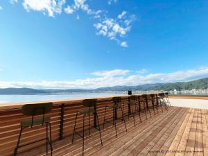 uma fila de bancos de bar num deque com vista para a água em Rako Hananoi Hotel em Suwa