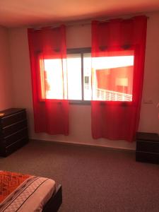 a bedroom with red curtains and a bed and a window at Chez ZAKARIA EDDOKKALY in Meknès