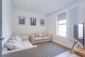 a white living room with a couch and a tv at The Stanley Maisonette in Teddington