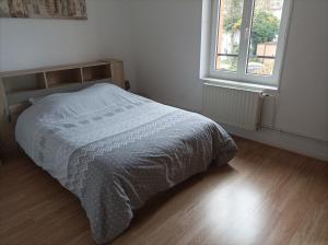 uma cama num quarto branco com piso em madeira em A l'ombre du lilas em Épinal