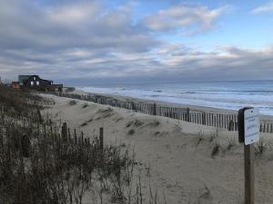 a beach with a fence and a house and the ocean at BlackBeard's Retreat - Historic and Pet Friendly cottage in Kitty Hawk